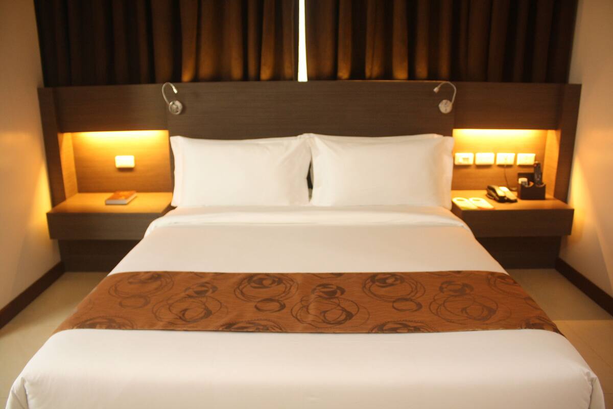 Ein Hotelzimmer mit einem großen Bett, zwei Nachttischen und einem Kopfteil mit integrierter Beleuchtung.