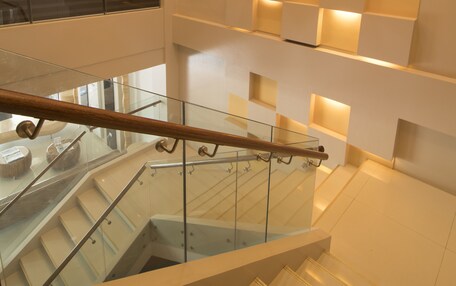 A modern interior with a glass staircase, a woven light fixture, and illuminated wall panels.