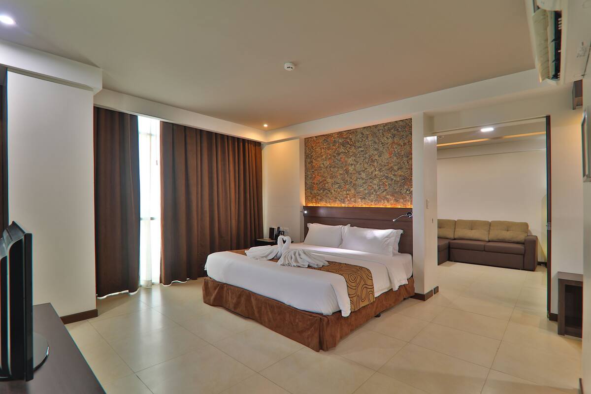Ein Hotelzimmer mit einem großen Bett, einer Couch, einem Flachbildfernseher und einem an der Wand befestigten Kunstwerk.