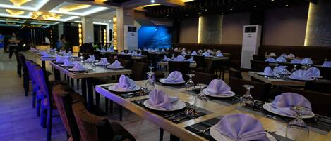 Un restaurante con varias mesas dispuestas, cubiertas con manteles blancos y servilletas moradas.