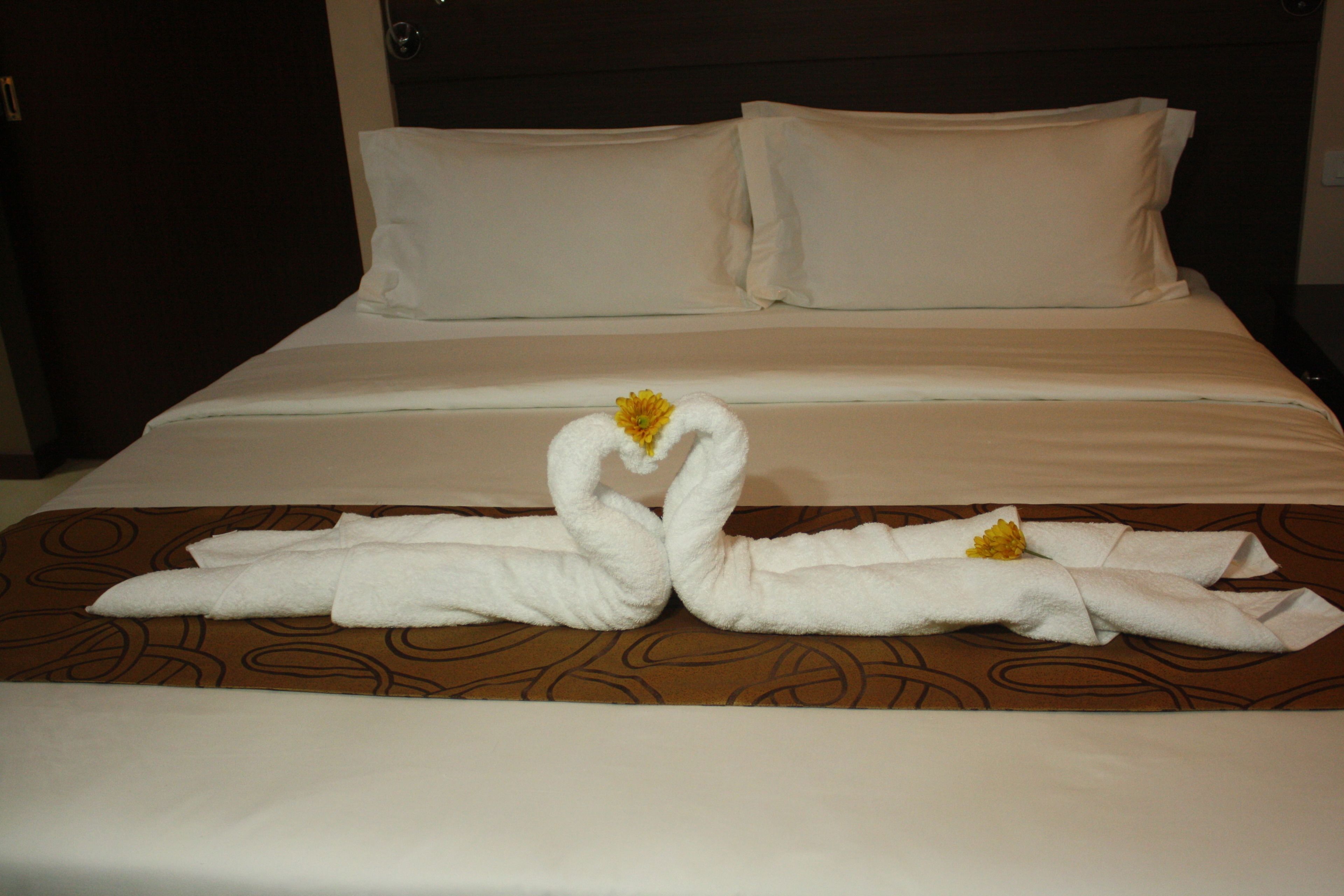 A hotel room with a bed featuring a brown patterned bedspread and two towels arranged in a swan shape with yellow flowers.