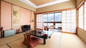 A traditional Japanese room with tatami flooring, a low table with a television, and sliding doors leading to a balcony with a mountain view. - Gorakan (Hakone)