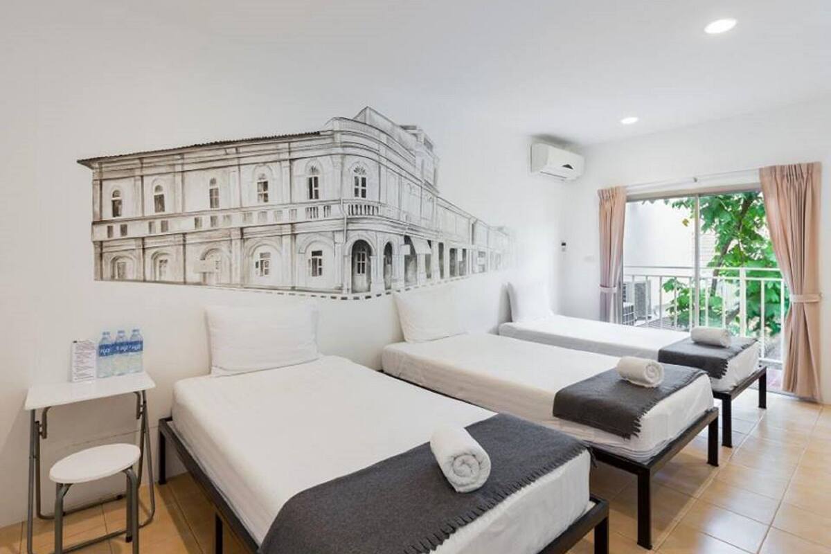 A hotel room with two beds, a small table, and a wall mural of a building.