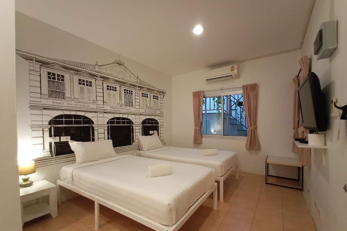 A hotel room with two beds, a small table, a TV, and a window with curtains.