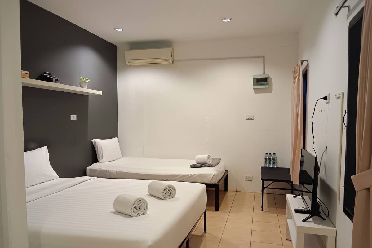 A hotel room with two beds, a desk, a TV, and an air conditioning unit.