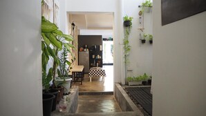 A narrow hallway with potted plants on both sides, leading to a dining area with a checkered tablecloth. - Chino Town Gallery Alley (Phuket)