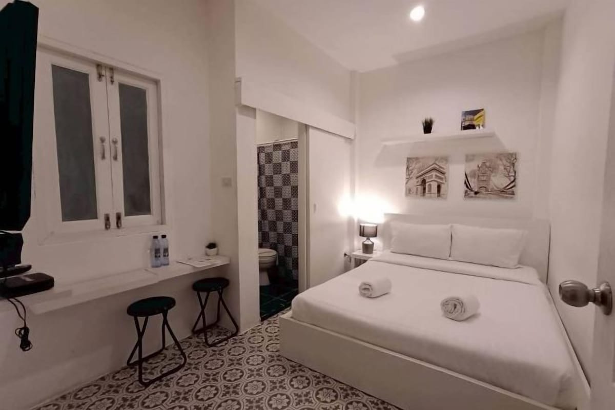 Un dormitorio con cama, mesita de noche, espejo, ventana y puerta.