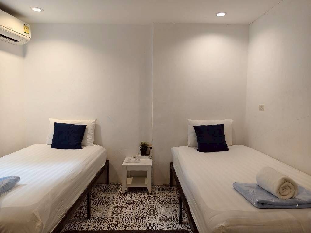 A room with two beds, a small table with a plant, and an air conditioning unit.