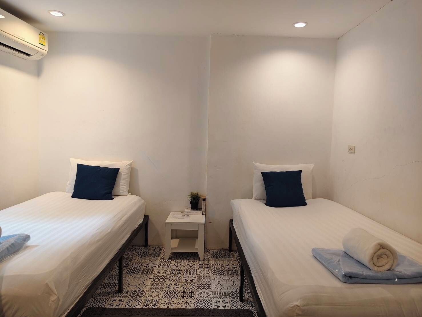 Una habitación con dos camas individuales, una mesita de noche con una planta y un suelo con estampado.