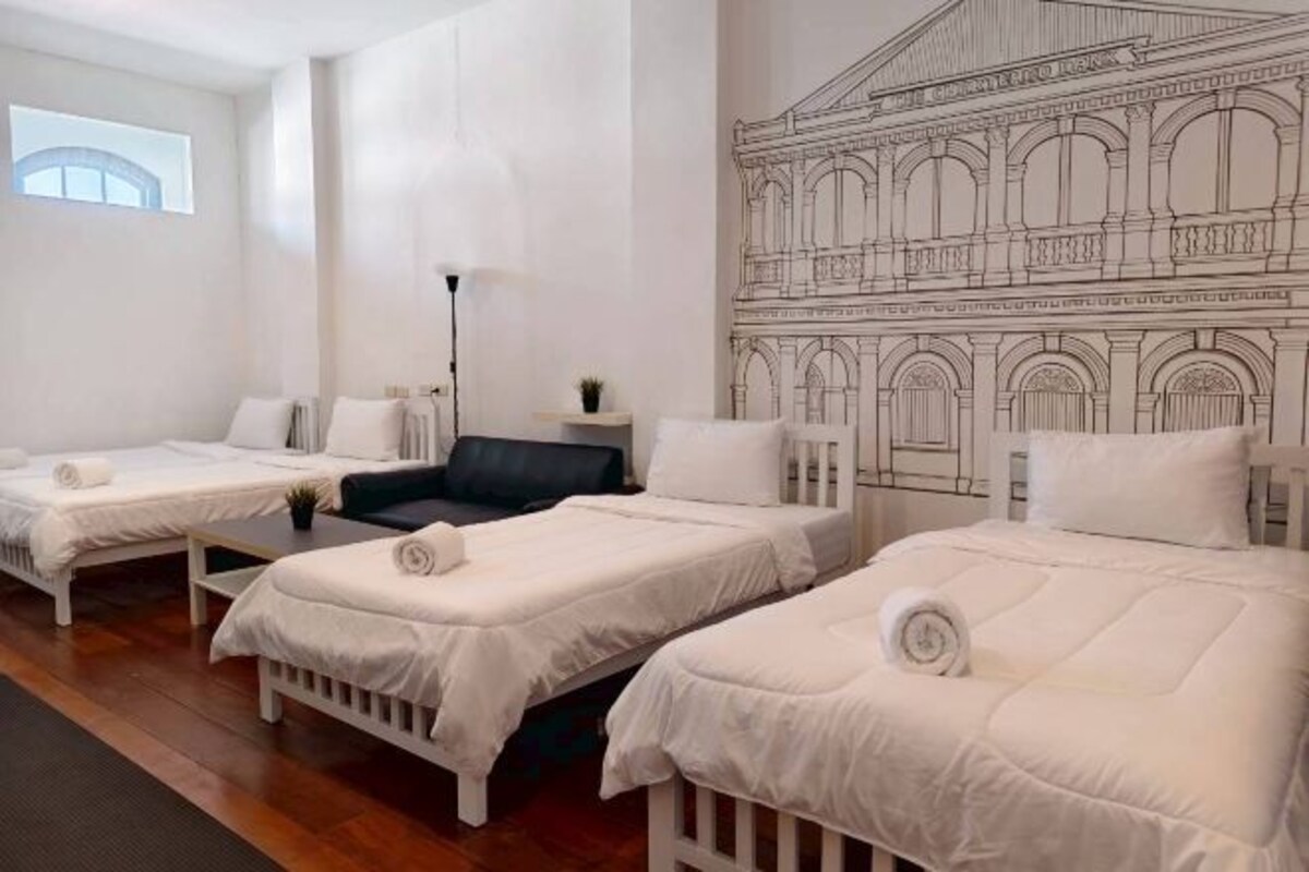 A hotel room with three single beds, a black chair, a desk, and a large wall mural.