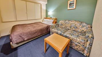Ein Hotelzimmer mit zwei Betten, einem Schlafsofa, einem kleinen Tisch, einer Lampe und einem Bild an der Wand.