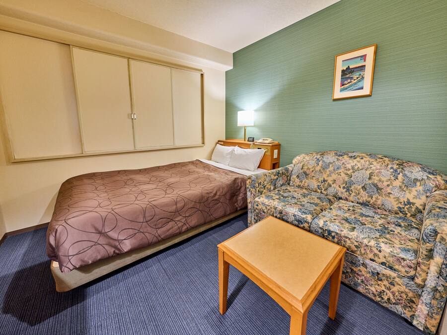 Ein Hotelzimmer mit zwei Betten, einem Schlafsofa, einem kleinen Tisch, einer Lampe und einem Bild an der Wand.