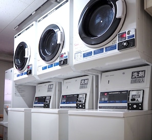 A row of front-loading washing machines with control panels and a coin-operated dispenser. - Smile Hotel Tokyo Shinkoiwa (Tokyo)