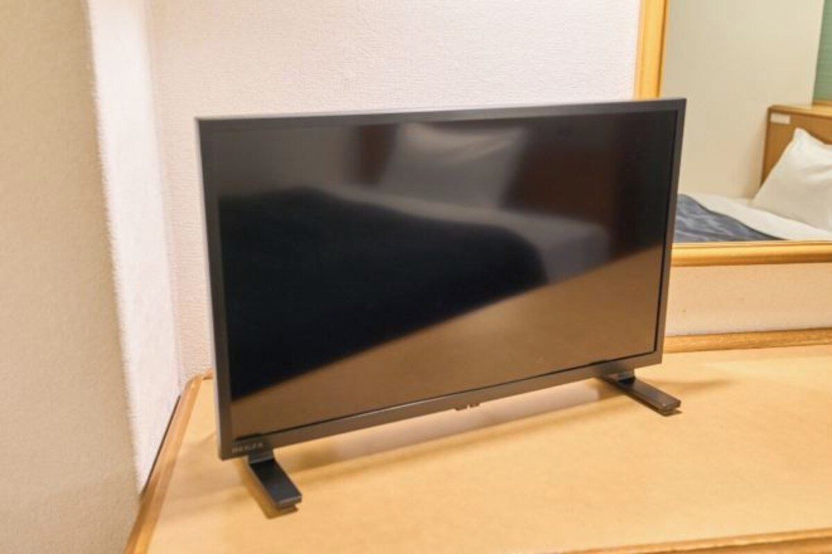 A flat-screen TV on a wooden stand in a room with a bed and a mirror.