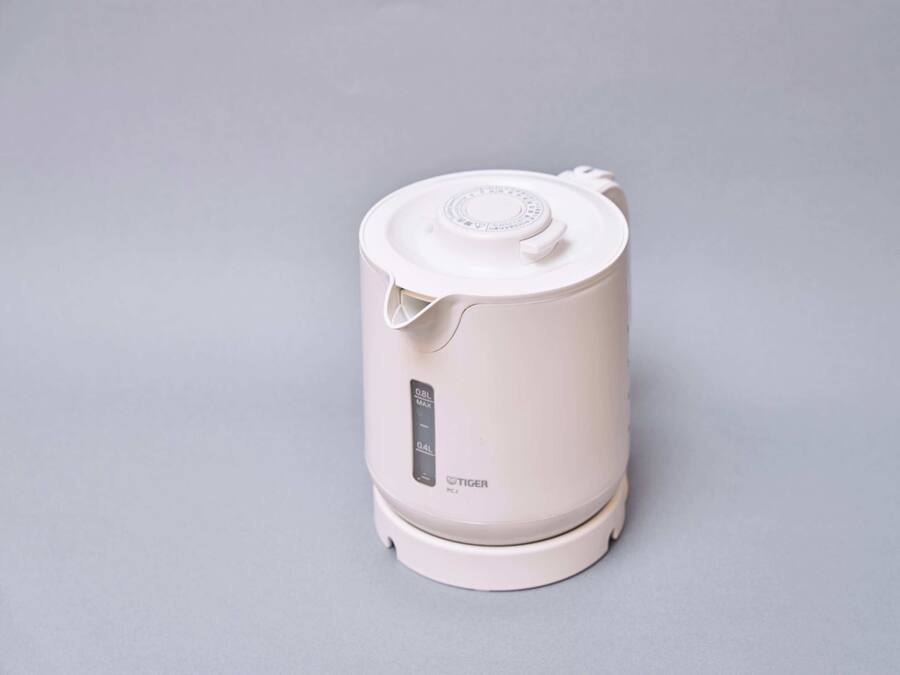 A white, cylindrical, portable coffee maker with a lid and a control panel, placed on a flat surface.