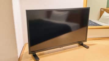 Un televisor de pantalla plana sobre un soporte en una habitación con piso de madera y pared blanca.
