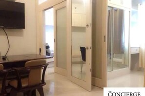 Una habitación de hotel con zona de comedor, televisión y puerta de vidrio que da a otra habitación.