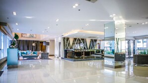 En rummelig lobby med et moderne design, der indeholder et siddeområde med sofaer og en kaffestation.