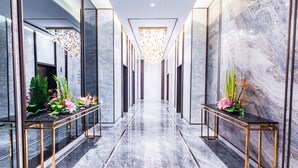 A hallway with marble floors and walls, flanked by two tables with floral arrangements. - Nade Hotel (Hangzhou)