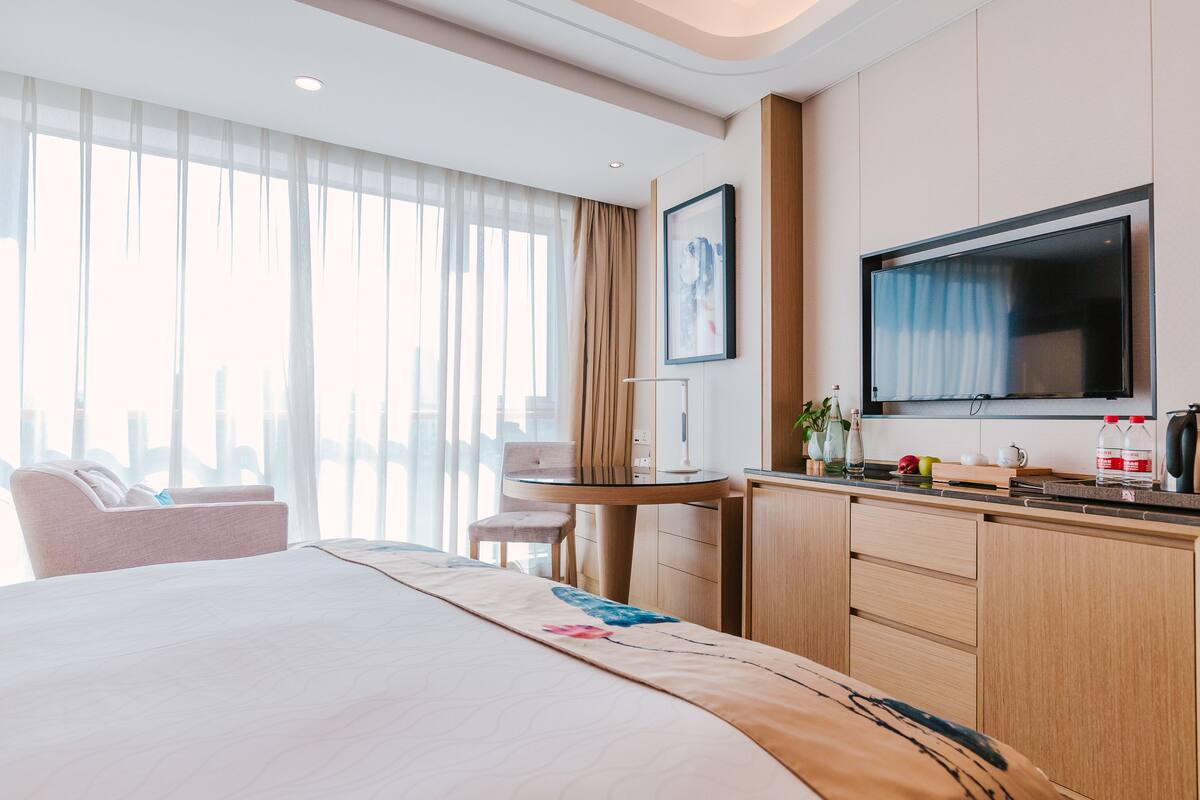 A hotel room with a bed, a desk, a chair, a TV, and a window with curtains.