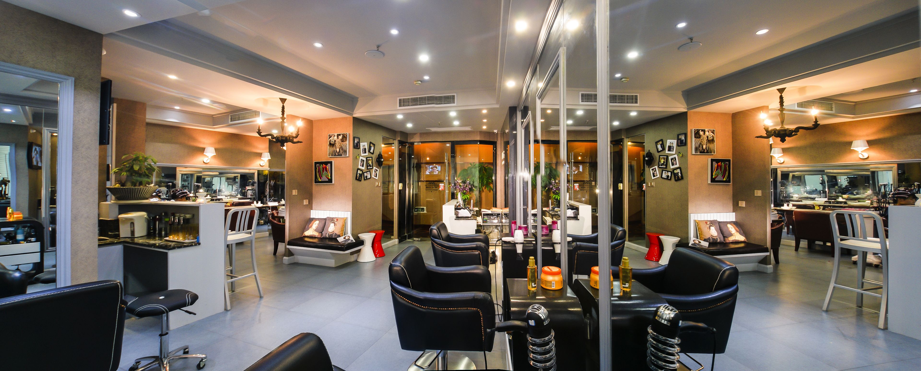 Un salón de belleza moderno con paredes de espejo, sillones de cuero negro y una recepción central.