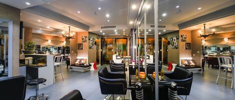 Un salón de belleza moderno con paredes de espejo, sillones de cuero negro y una recepción central.