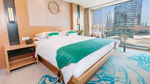 A hotel room with a large bed, a bedside table with a phone, a view of a cityscape through large windows, and a balcony with a table and chairs. - Nade Hotel (Hangzhou)