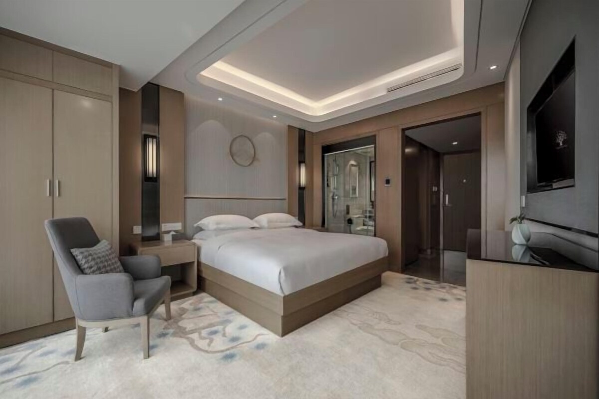 A modern bedroom with a bed, a chair, a desk, a TV, and a wardrobe.