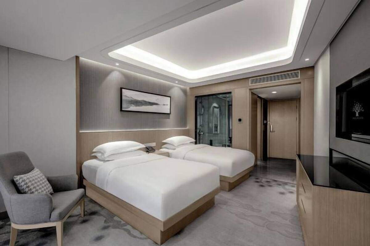 A modern hotel room with two beds, a TV, a chair, and a ceiling light.