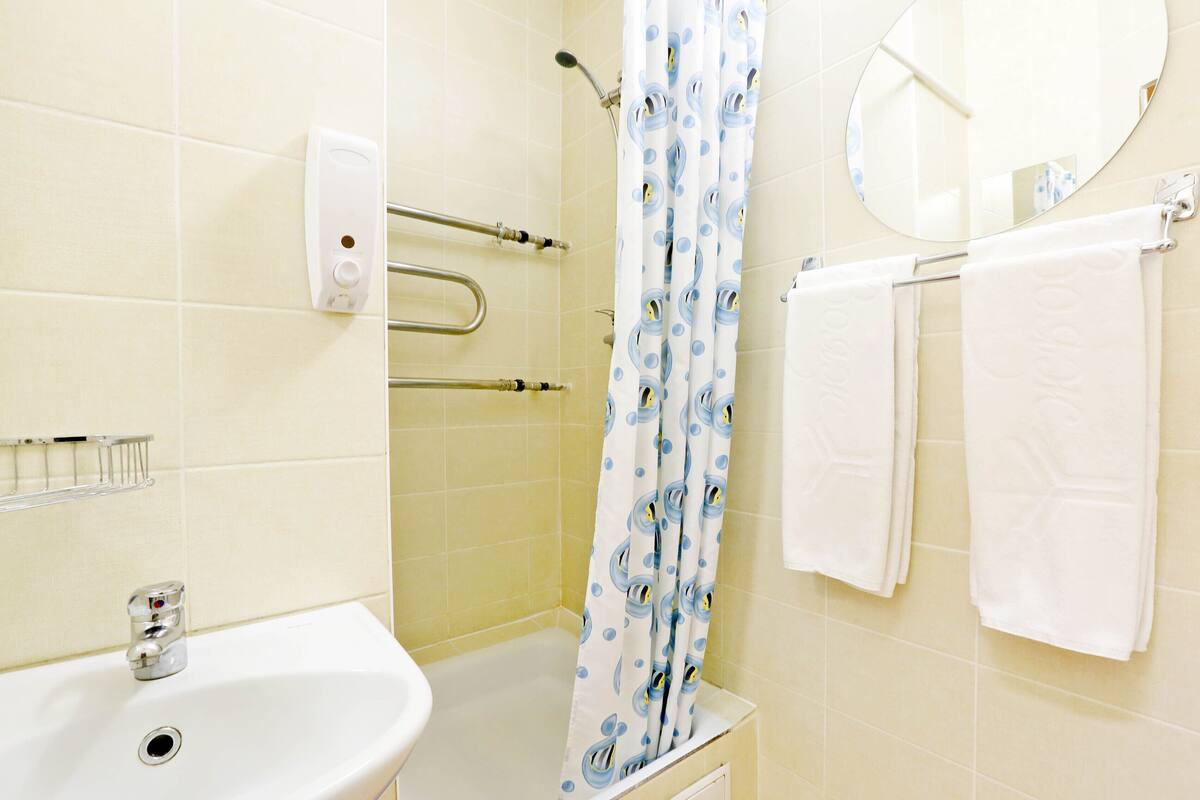 A bathroom with a sink, a shower with a blue polka dot curtain, a mirror, and two white towels on a rack.