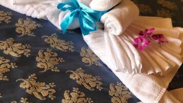Una toalla doblada con un lazo azul y flores rosas, colocada sobre una cama con una colcha azul oscura estampada.
