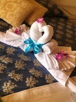 Una toalla doblada con un lazo azul y flores rosas, colocada sobre una cama con una colcha azul oscura estampada.