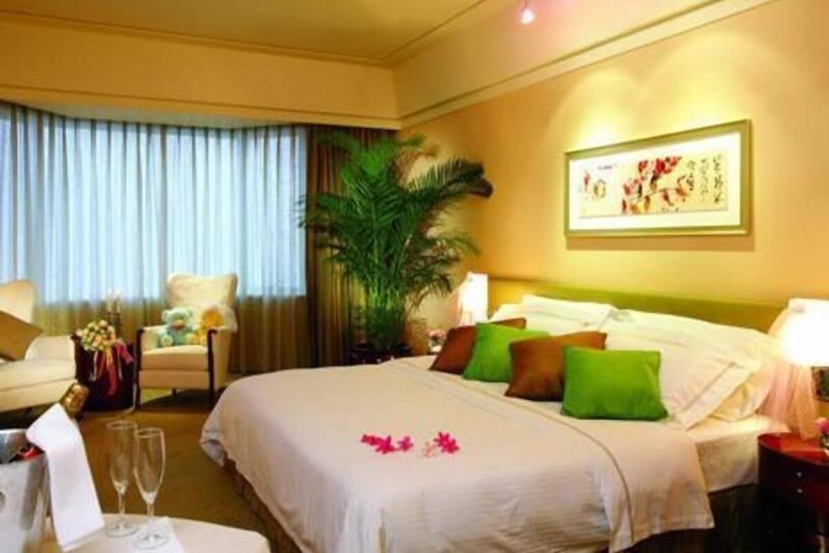 Ein Hotelzimmer mit einem Bett, einem Sessel, einem Tisch mit Vase und Gläsern, einer Pflanze und einem gerahmten Bild an der Wand.