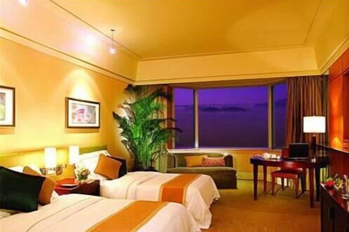 Ein Hotelzimmer mit zwei Betten, einem Schreibtisch, einem Stuhl, einer Pflanze und einem Fenster mit Blick.