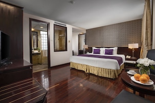 Una habitación de hotel con una cama grande, televisión, escritorio con lámpara y un jarrón con flores.