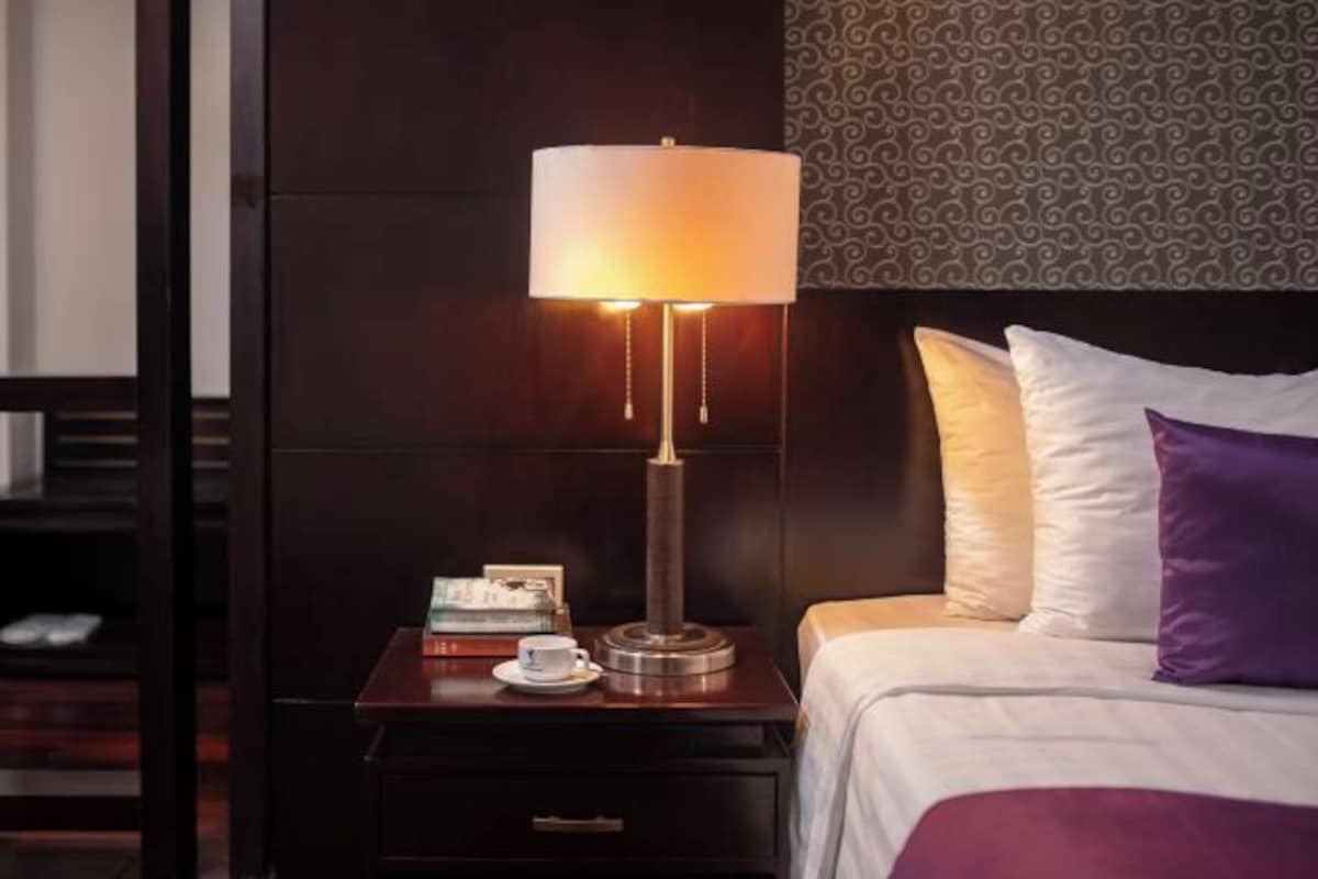 Quarto de hotel com cama, mesa de cabeceira, abajur e parede estampada.