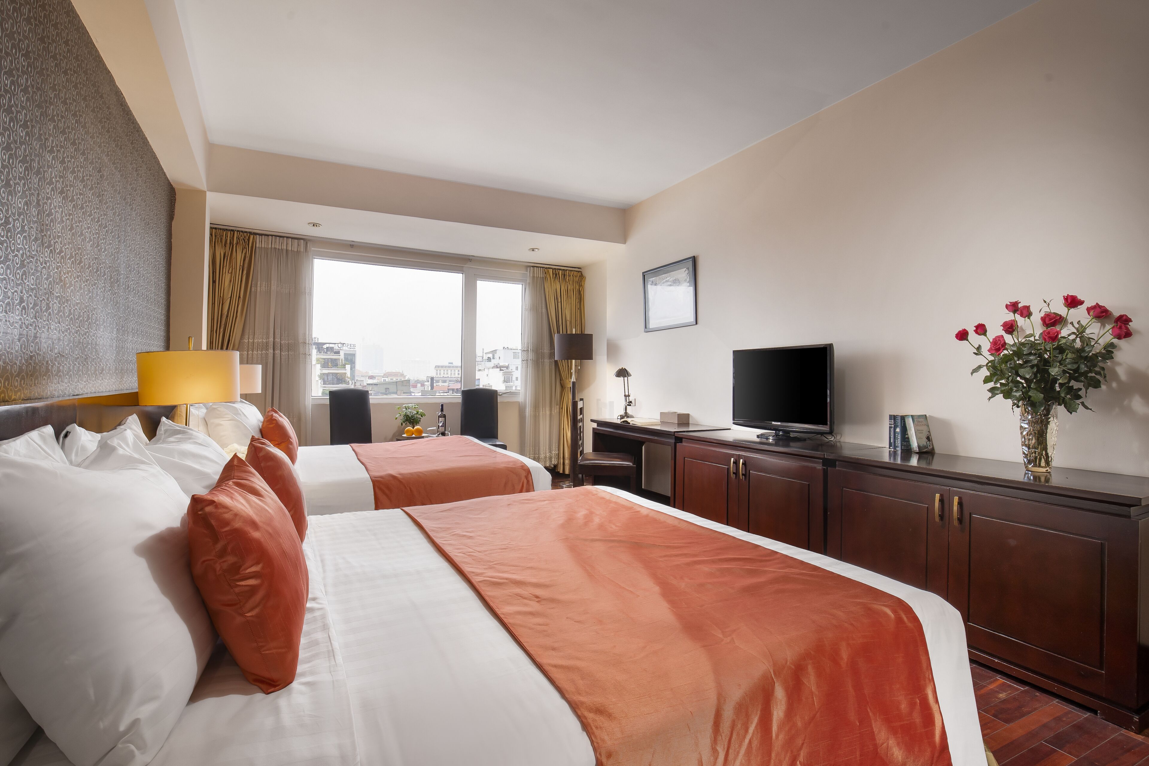 A hotel room with two beds, a TV, a desk, and a window with curtains.