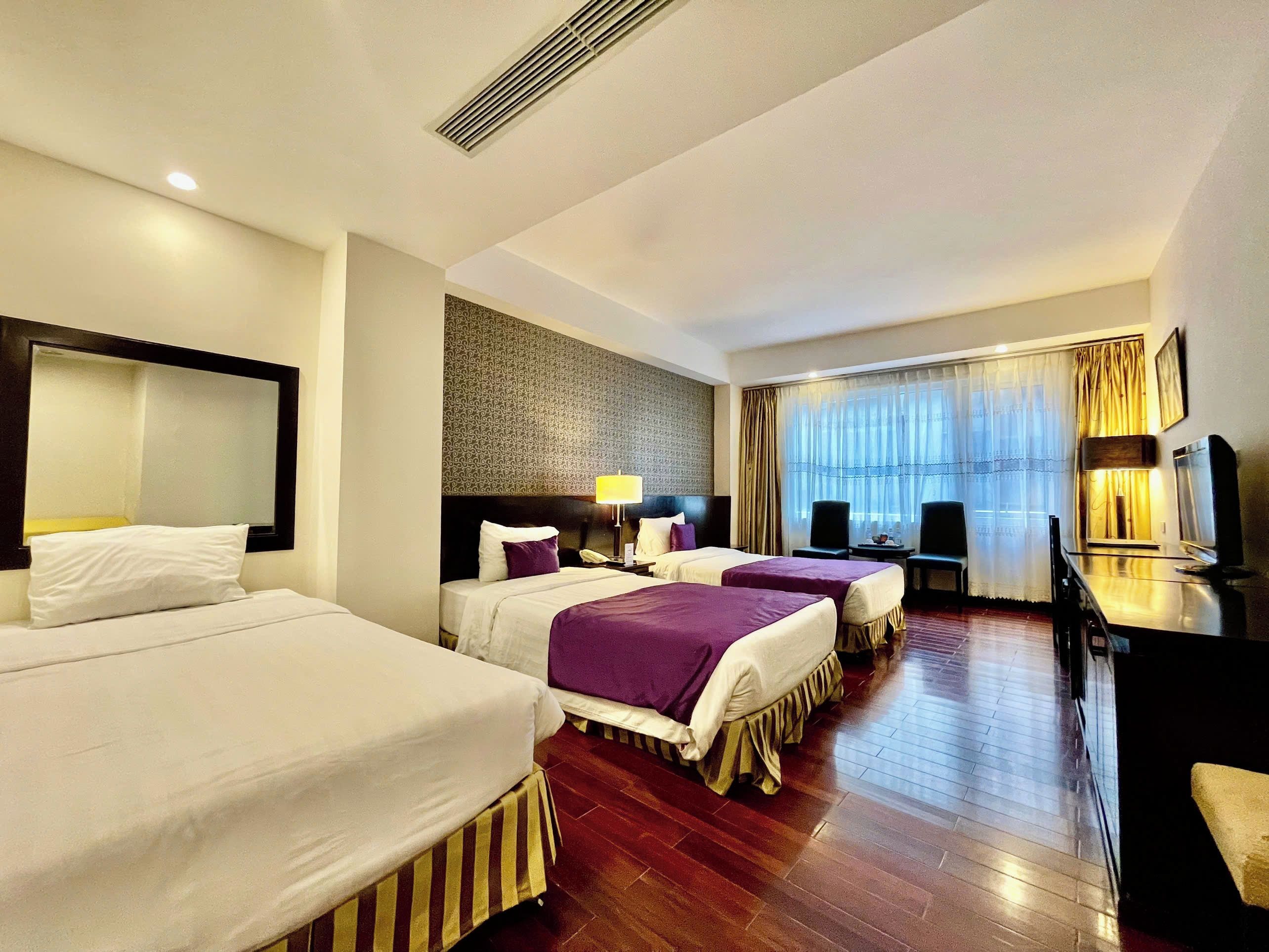 A hotel room with two beds, a desk, a chair, a television, and a large window with curtains.