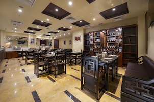 Un restaurante con varias mesas y sillas, una estantería para vinos y una barra.