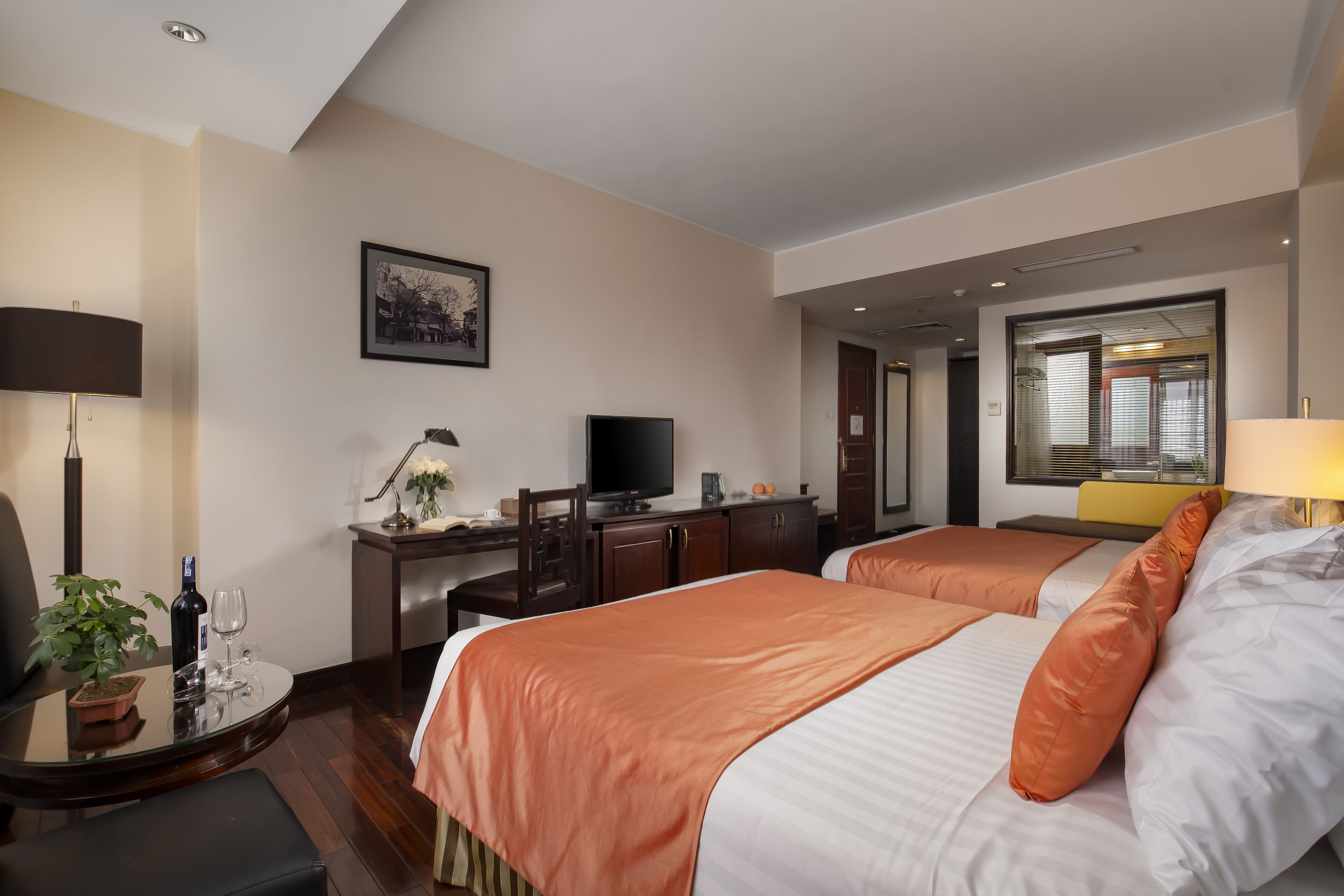 A hotel room with two beds, a desk with a computer, a TV, and a potted plant.