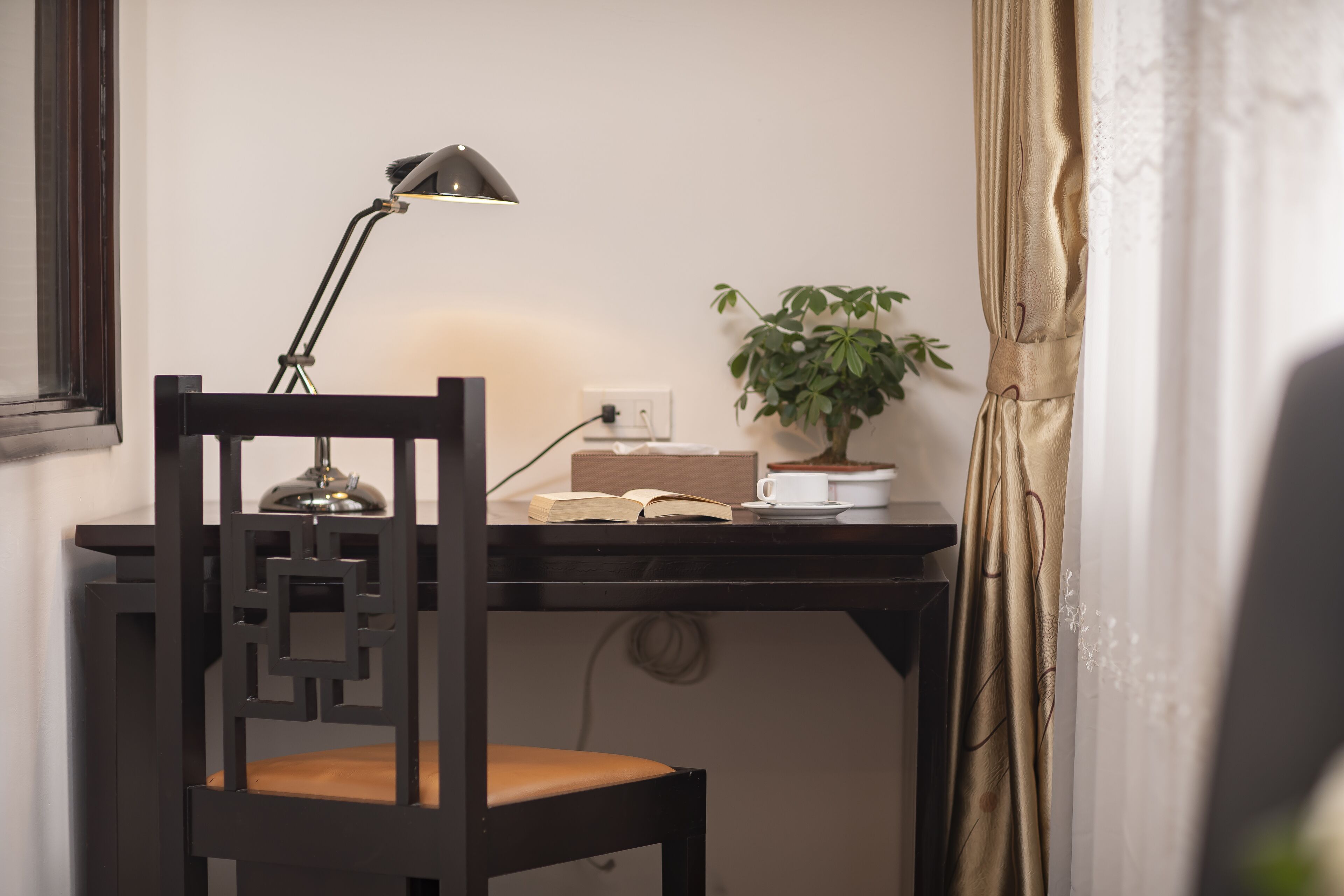 A desk with a lamp, a chair, a plant, and a book.