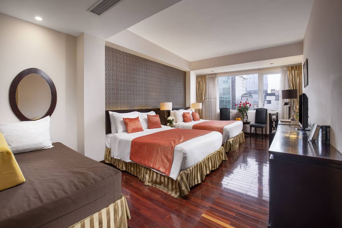 A hotel room with two beds, a desk, a TV, and a large window with a view of the city.