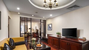 A modern living room with a yellow sofa, a glass coffee table, a TV on a wooden cabinet, and a chandelier. - TK123 Hanoi Hotel (Hanoi)
