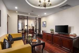Una sala moderna con un sofá amarillo, una mesa de centro de cristal, un televisor sobre un mueble de madera y una araña.