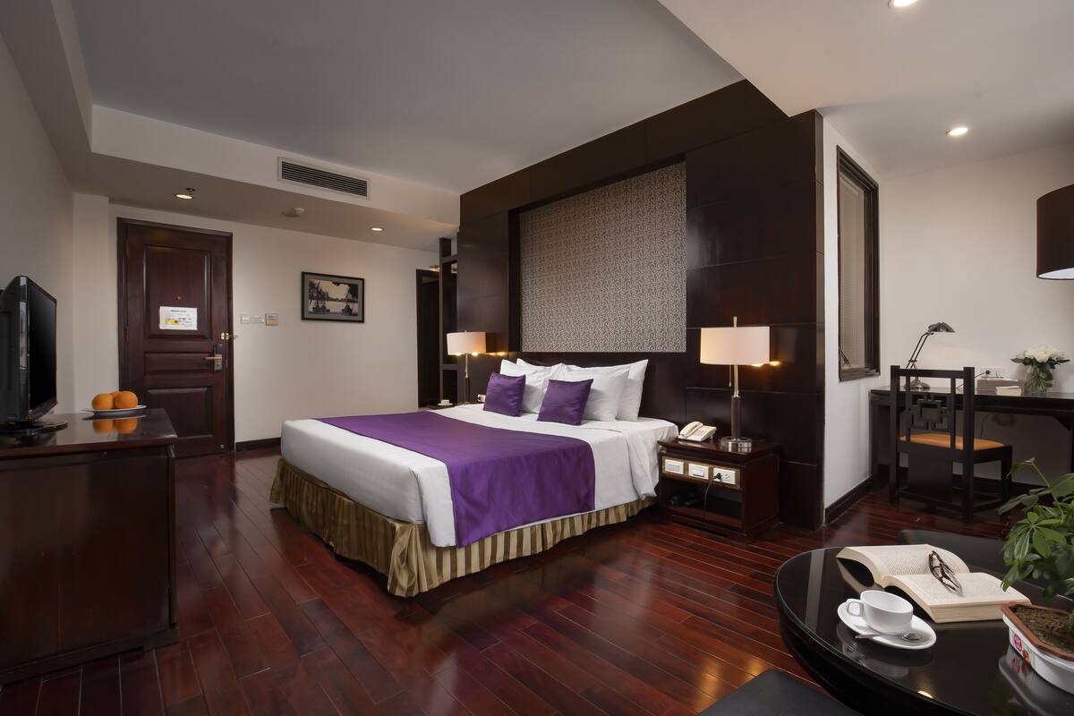 A hotel room with a large bed, a desk, a chair, a television, and a plant.