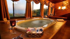 Een spa-kamer met een jacuzzi, een glas rode wijn, kaarsen en een mandje met toiletartikelen.