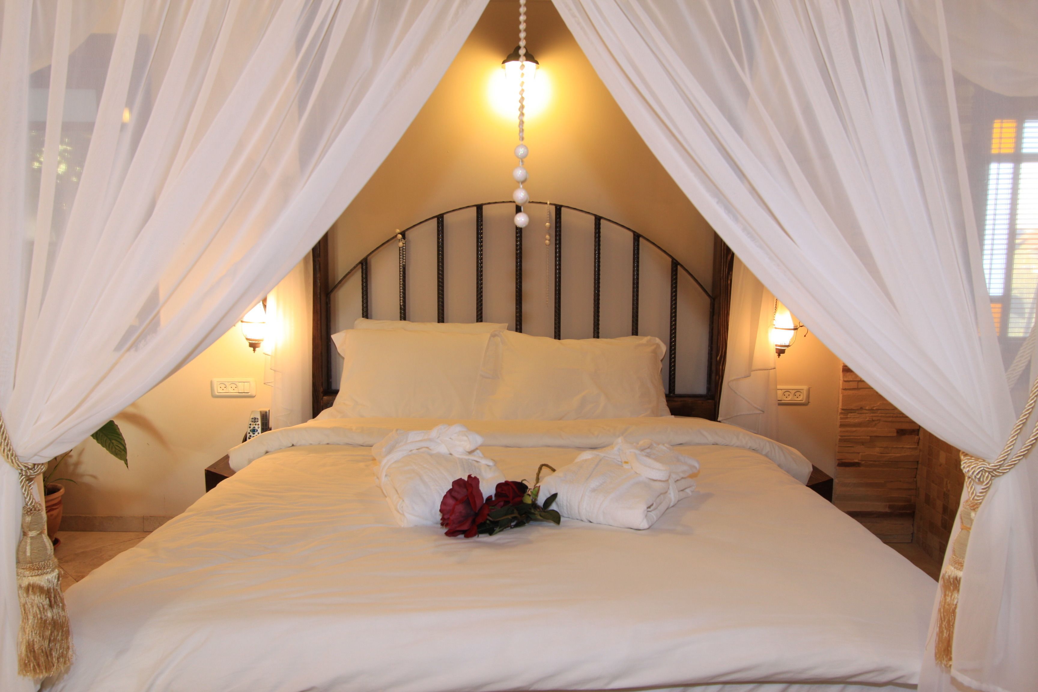 A neatly made bed with white linens, a bouquet of red roses, and a canopy.