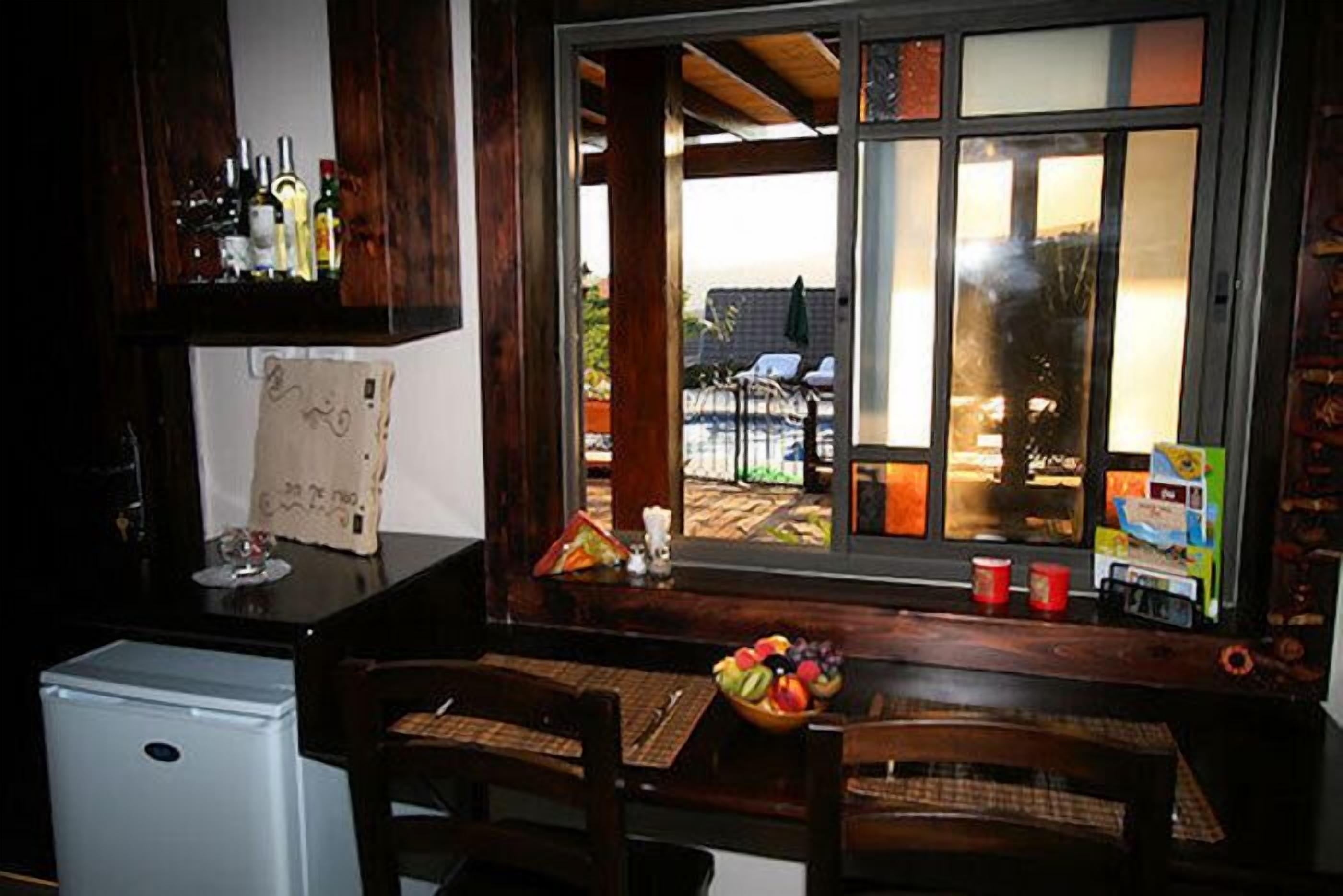 A kitchen with a refrigerator, a dining table with chairs, a window with a view of the outside, and various kitchen items on the counter.