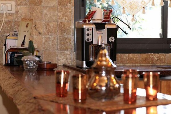 Una encimera de cocina con una cafetera, un centro de mesa decorativo de vidrio y una ventana con vistas a la vegetación.