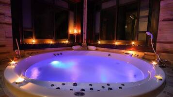 Een hottub met kaarsen eromheen, gelegen in een kamer met houten wanden en ramen.